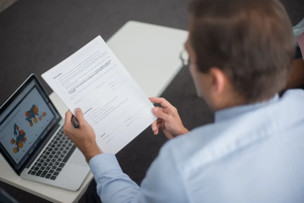 Persona revisando un documento junto a un portátil antes de aprobar una respuesta preparada por un agente de IA