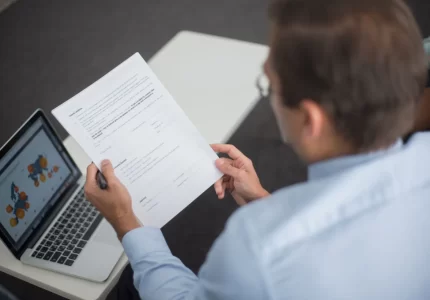 Persona revisando un documento junto a un portátil antes de aprobar una respuesta preparada por un agente de IA